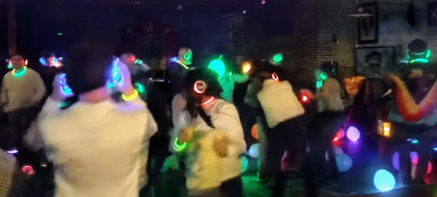 Crowded dance floor at a silent disco, headsets glowing green, red, and blue