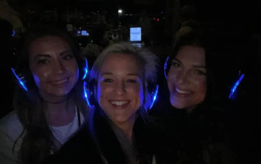 Three friends smiling in glowing blue silent disco headphones