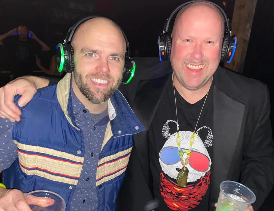Two friends laughing in silent disco headsets at the first party